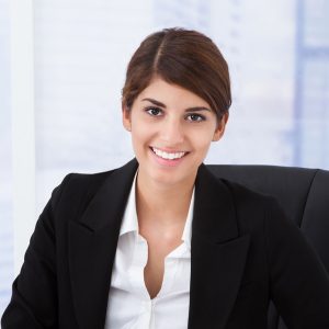 Portrait of confident young businesswoman using calculator at office desk